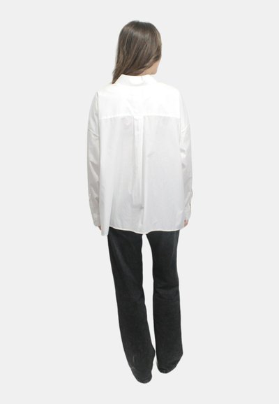 Camicia bianca in cotone con design a yoke sul retro, maniche lunghe e taglio rilassato, abbinata a pantaloni neri a gamba larghi.