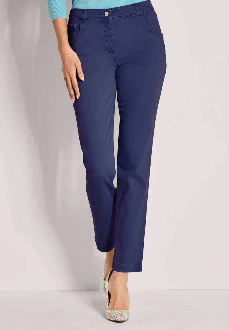 Marineblauwe, rechte broek met een gladde textuur, voorzakken en een knoopsluiting. Gemaakt in combinatie met veelkleurige, gemusterde hakken.