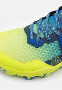 Lebendige gelbe und blaue Sportschuh mit einer strukturierten Oberseite, gemusterten Schnürsenkeln, schützendem Zehenkappen und multidirektionalen Traktionsspikes.