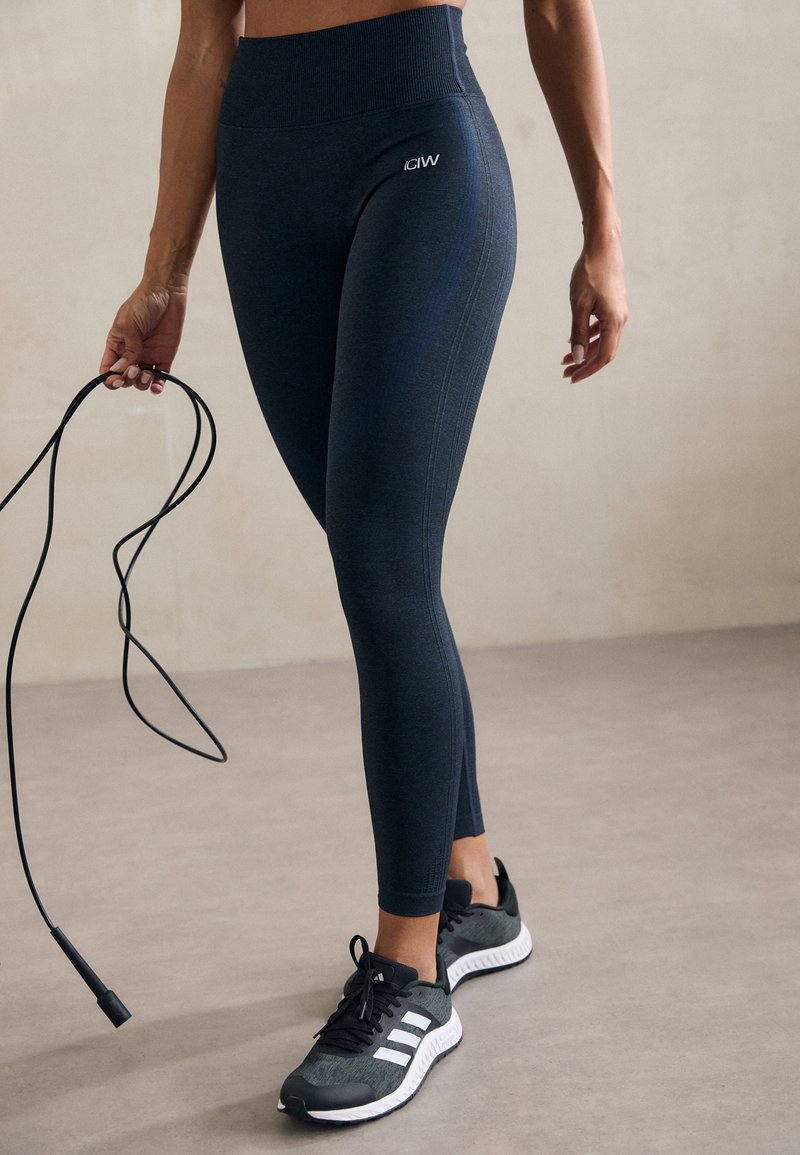 Höga mörkblå leggings med en mjuk textur och sidstygsdetaile, matchade med svarta träningsskor med vita ränder.