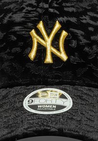 Căciulă de baseball din catifea neagră cu un logo al New York Yankees brodat cu fir auriu. Curea reglabilă și etichetă rotundă care indică mărimea și ajustarea.