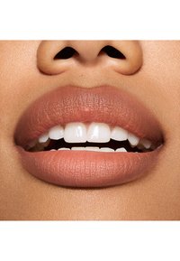 Gros plan sur des lèvres avec une finition mate nude, montrant une texture lisse, une forme bien définie, et des dents blanches avec un léger écart.