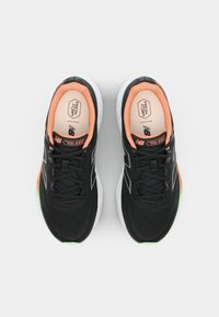 Black athletic shoes with a mesh upper, orange inner lining, white midsole, and green, orange, and yellow accents on the sides.