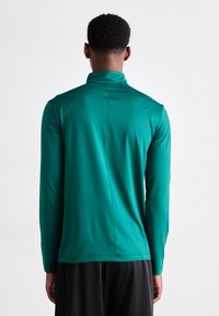 Maglietta sportiva verde a maniche lunghe con colletto alto e texture liscia. Presenta cuciture piatte e un design aderente. Vista posteriore mostrata.