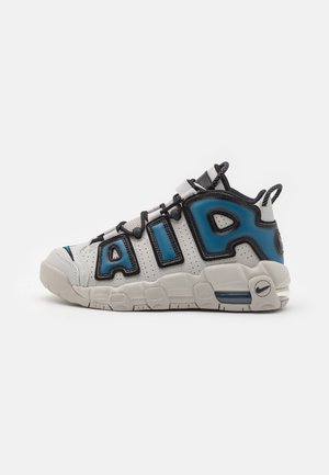 Weiß-blauer Nike Air Sneaker mit großem "AIR" Schriftzug an der Seite, schwarzen Schnürsenkeln und sichtbarer Air-Dämpfung in der Sohle, dargestellt im linken Profil.