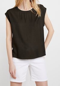 Mörkgrön kortärmad topp i ett mjukt, slätt tyg med rund halsringning. Buren med vita shorts som har en avslappnad passform och minimalistisk design.