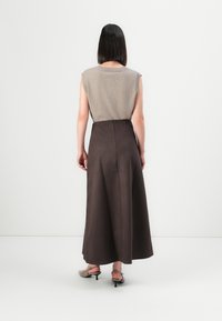 Woman with straight black hair wearing a beige sleeveless top, dark brown midi skirt, and taupe kitten-heeled slingback shoes standing facing away.