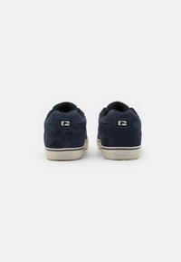 Navy blue suede sneakers with a textured finish, cream rubber soles, and a low-profile design. Features logo accents on the heel.