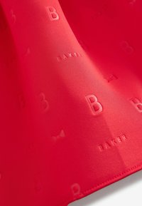 Tissu rouge présentant une texture lisse avec des motifs en relief de la lettre "B" et du mot "BAKER". Des motifs de nœuds subtils sont également inclus.