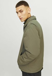 Green lightweight jacket with a classic collar, side pockets, and a smooth texture. The design features a relaxed fit and subtle stitching details.