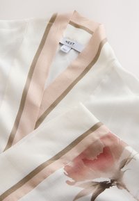 Vit och beige randig plagg med blommönster nära ärmen och en klädetikett med texten "NEXT."