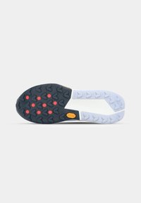 Semelle de sneaker en noir et blanc présentant un motif texturé, des accents rouges et un logo jaune. Le design inclut des éléments de traction clairs.
