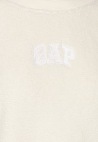 Sweter z polarowego materiału w kolorze kremowym o miękkiej fakturze, z haftowanym logo "GAP" w kolorze białym na klatce piersiowej.