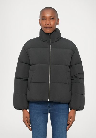 Schwarze Pufferjacke mit hohem Kragen, gepolstertem Design, Reißverschluss und elastischen Bündchen, kombiniert mit blauen Jeans. Glatte, leichte Textur.
