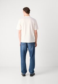 Light beige short-sleeve t-shirt with a classic fit, paired with blue straight-leg jeans, both featuring simple design and minimal detailing.