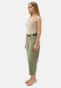 Canotta beige a coste abbinata a pantaloni tapered verde oliva a vita alta, dotati di tasche laterali e una cintura nera con hardware dorato.