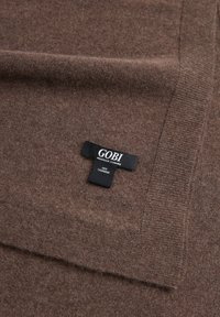 Écharpe en cachemire brun avec une texture douce, ornée d'une étiquette noire sur laquelle est brodé "GOBI" et "100% CACHEMIRE".