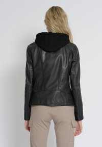 Schwarze Lederjacke mit Kapuze, taillierte Passform, glatte Textur, Nahtdetails und langen Ärmeln. Getragen mit hellbeigen Cargo-Hosen.