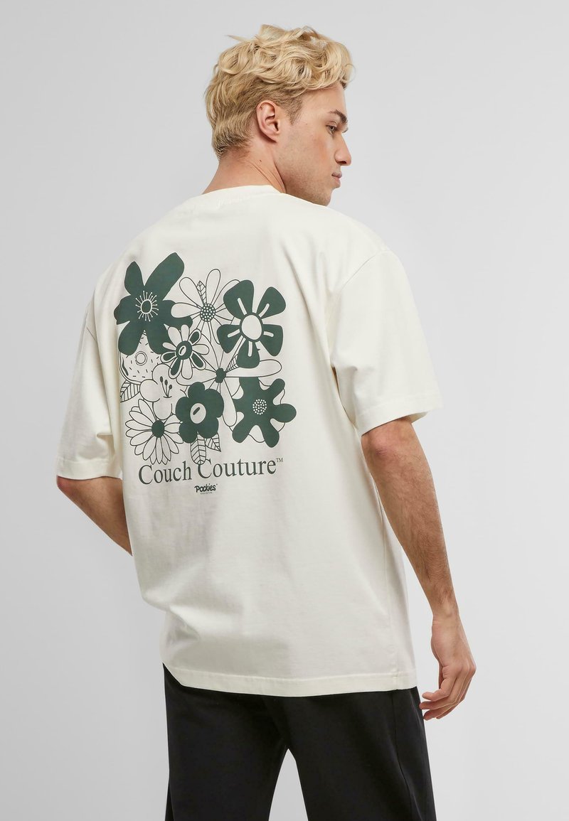 Krems kr短s piedurkņu T-krekls ar zaļu ziedu rakstu aizmugurē, centrā ar tekstu "Couch Couture™".