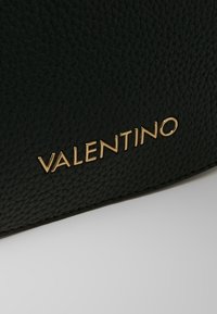 Svart texturerad läderväska med en guldprägling av "VALENTINO"-logotypen på framsidan. Kompakt design med rena linjer och subtila detaljer.