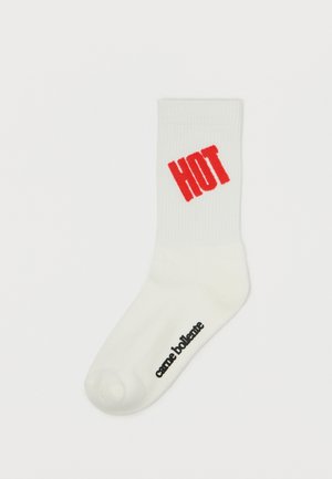 Chaussette en coton blanche avec une texture côtelée, comportant le mot "HOT" en lettres rouges en gras sur le côté et un logo noir au niveau du orteil.
