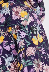 Stof met bloemenpatroon met paarse, gele en roze bloemen, met illustraties van kittens. Inclusief een zwart "ZIGZAG" logo patch.