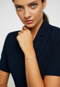 Bracciale d'argento con una pietra centrale rotonda, con delicate maglie a catena e design minimalista, indossato su un polso in contrasto con un outfit scuro.