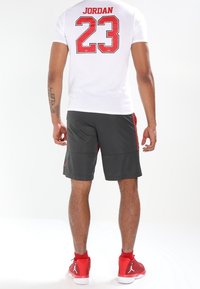 Vit t-shirt med "JORDAN 23" i rött på baksidan, i kombination med mörkgrå shorts med röda sidostråk och röda sportskor.