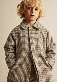 Bølgeret på jakke i beige og brun, med krave og knaplukning, lavet af struktureret stof.