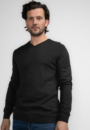 Suéter en gris oscuro, con cuello en V, hecho de una tela suave y de mangas largas. Detalles de puños y dobladillo acanalados. Lleva puesto sobre unos jeans azules.