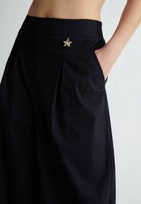Czarne spodnie o szerokich nogawkach z gładką fakturą, z dekoracyjnym guzikiem w kształcie gwiazdy i kieszeniami bocznymi dla dodatkowej funkcjonalności.