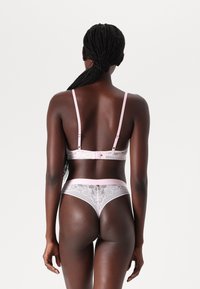 Lace bra and thong set in pink with adjustable straps and floral pattern. Back view highlights intricate lace texture and branded waistband.