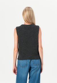 Pull sans manches gris foncé à texture côtelée, col rond et ourlet, associé à un jean bleu à taille haute et jambes larges.