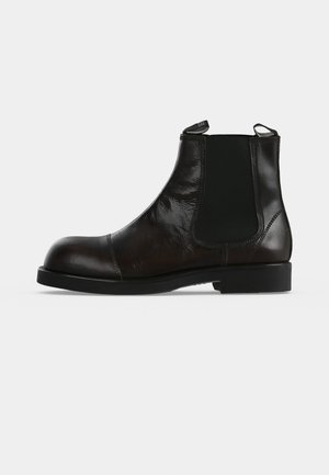 Bottine Chelsea en cuir noir avec empiècements latéraux élastiques, tirettes, bout arrondi et talon bloc bas.