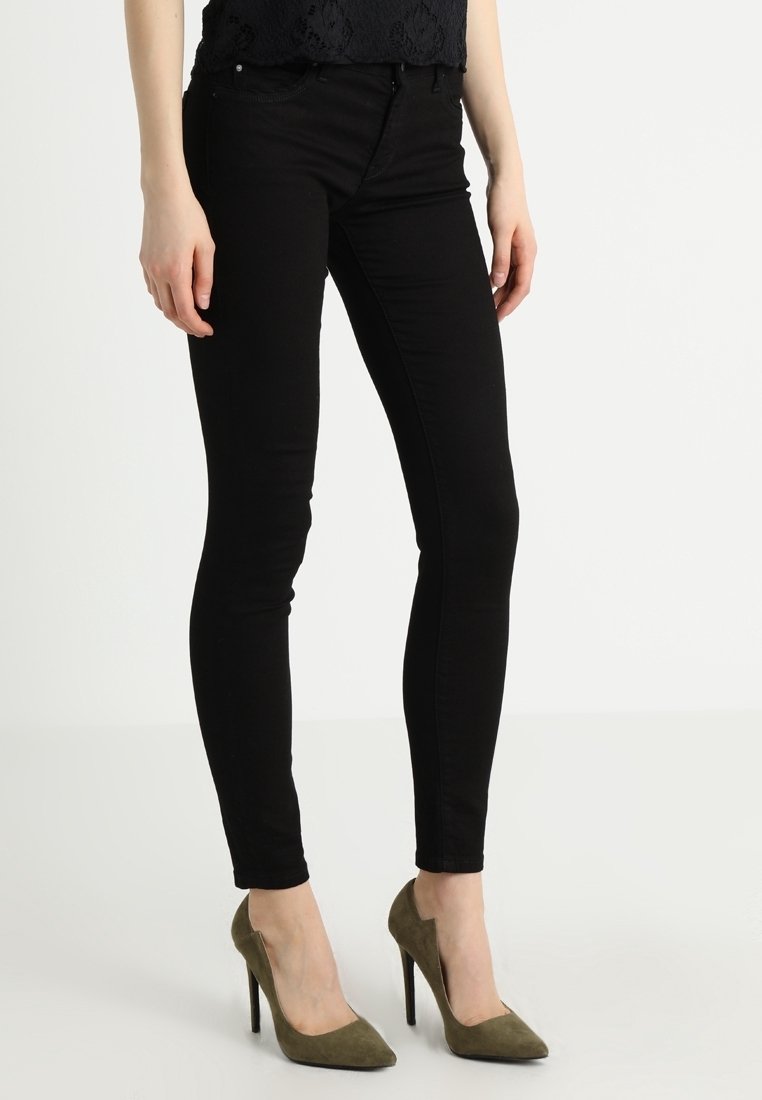 Jeans skinnies negros con una textura suave, cintura alta y cinco bolsillos, combinados con zapatos de tacón altos en color verde oliva.