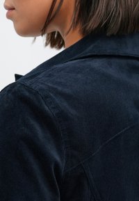 Μπλε μπουφάν από κορδονέ ύφασμα με υφή, διαθέτει ραμμένο γιακά και λεπτομέρεια στον ώμο, εμφανίζεται από το πλάι.