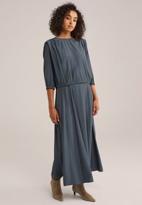 Robe longue grise à manches trois-quarts, taille froncée et silhouette fluide. Assortie à des bottines beige à bout pointu.