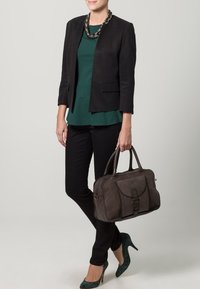 Svart blazer över en grön topp, kombinerad med svarta byxor och gröna mönstrade klackskor. En mörkbrun handväska med en strukturerad design.