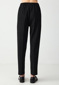 Zwarte broek met elastische tailleband en een taps toelopend ontwerp. Soepele textuur, plooien aan de achterkant en een cropped lengte boven de enkel.