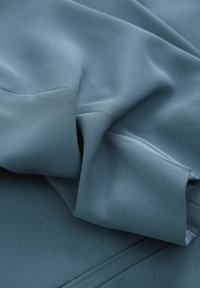 Tessuto blu dalla trama strutturata con una caduta morbida, presenta sottili coste e sezioni piegate, con bordi lisci e finitura opaca.