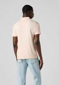 Kortärmad polo i ljusrosa bomull, med klassisk krage, avslappnad passform och subtila sidoflikar. Matchas med ljusblå jeans.