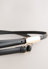 Czarny skórzany pasek o eleganckim wzornictwie, z złotym metalowym akcentem i gładką, prostokątną klamrą. Delikatna faktura i minimalistyczne elementy metalowe.