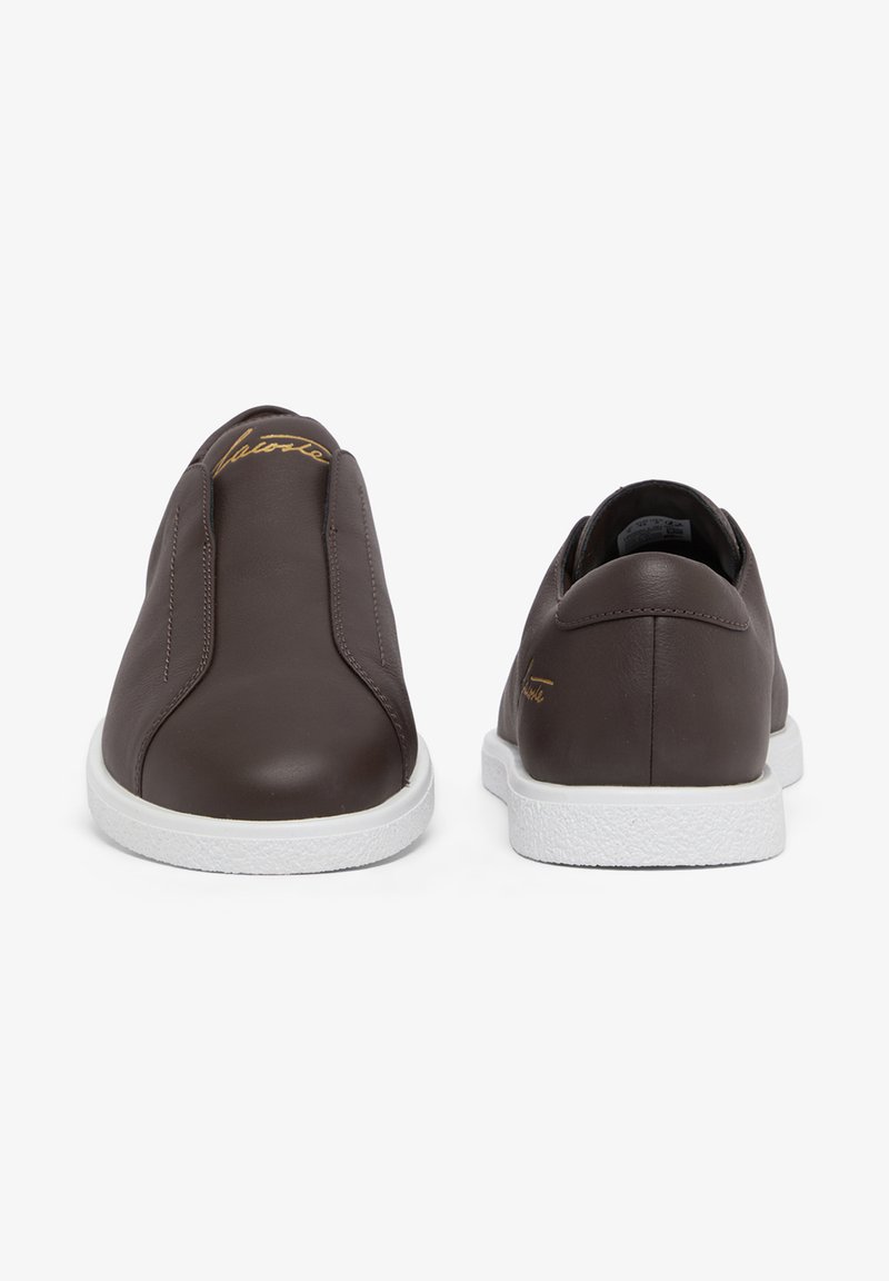 Coppia di sneakers slip-on in pelle marrone scuro con suole bianche, mostrate da davanti e da dietro, con delicati dettagli in scrittura dorata.