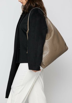 Braune Leder-Hobo-Tasche mit gestepptem Muster, zeigt eine lässige Form und einen einzelnen Schulterriemen, getragen zu einem schwarzen Mantel und weißen Hosen.