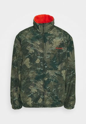 Veste zippée camouflage verte avec col montant, doublure en polaire orange, poignets élastiques, poches à l'avant et petit logo rouge sur la poitrine gauche.