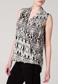 Bezramieniowa bluzka w czarno-białym kolorze z abstrakcyjnym wzorem, z falbanym przodem i miękkim teksturowanym materiałem.