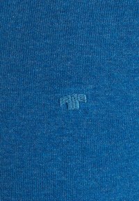 Tissu tricoté bleu avec une texture douce. Comprend un logo en relief subtil dans une teinte de bleu plus clair. Aucun motif ou élément métallique visible.