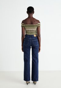 Off-the-shoulder green and beige striped knit top paired with dark blue high-waisted flared jeans featuring back pockets.