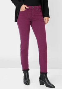 Jeans magenta con un corte slim, cuatro bolsillos, cierre frontal con botón y dobladillos enrollados. Combinados con botas negras hasta el tobillo.