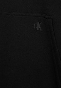 Tessuto di felpa nera con finitura texturizzata, con un piccolo logo 'cK' in rilievo nell'area della tasca.